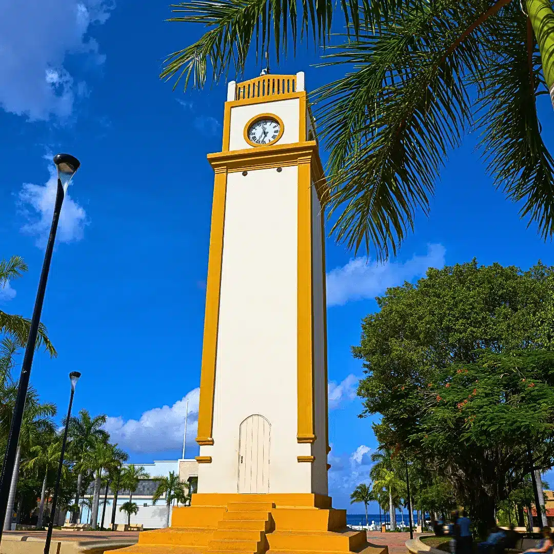 Local landmark: Cozumel clock tower and Caribbean Sea. Clock tower in Cozumel, lush trees, ocean view.