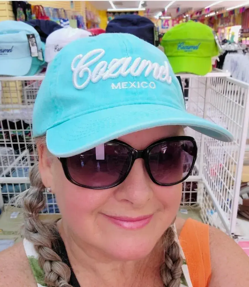 Lisa, a local, wearing a turquoise Cozumel hat with white lettering, sunglasses, and braided hair, ready to explore.