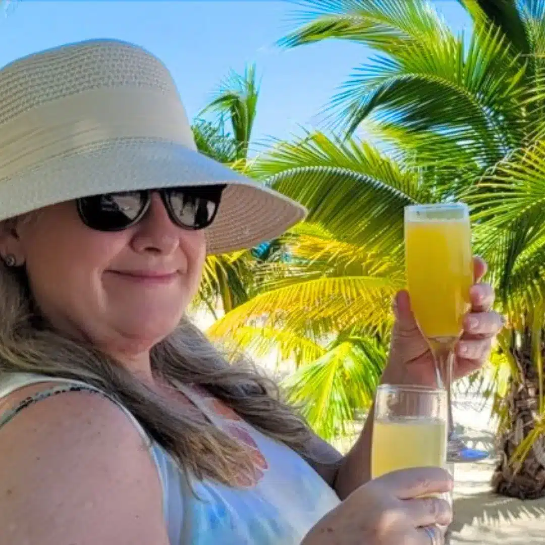 Lisa smiling and holding two mimosas, enjoying a 2-for-1 special.
